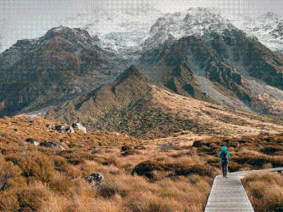 A hiker on a wooden boardwalk path heading toward snow-capped mountains